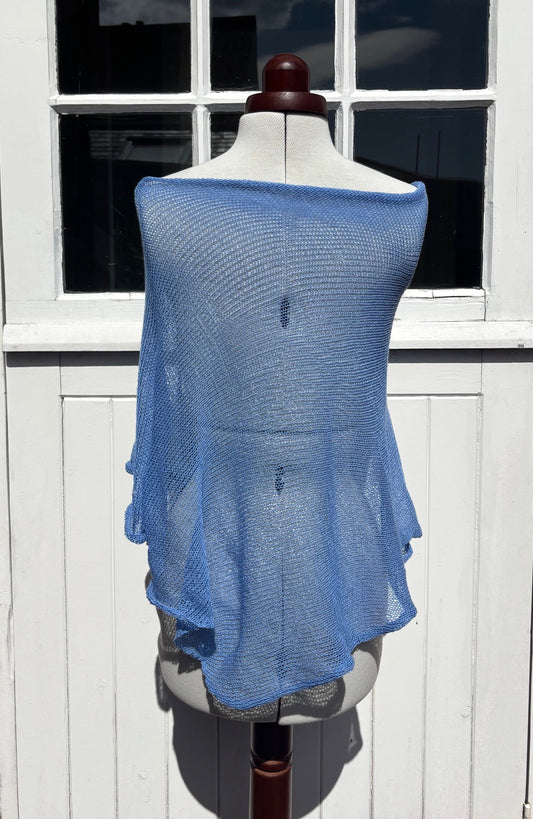 A light blue open-knit shawl or wrap draped over a dress form mannequin, set against a white paneled door with window panes.
