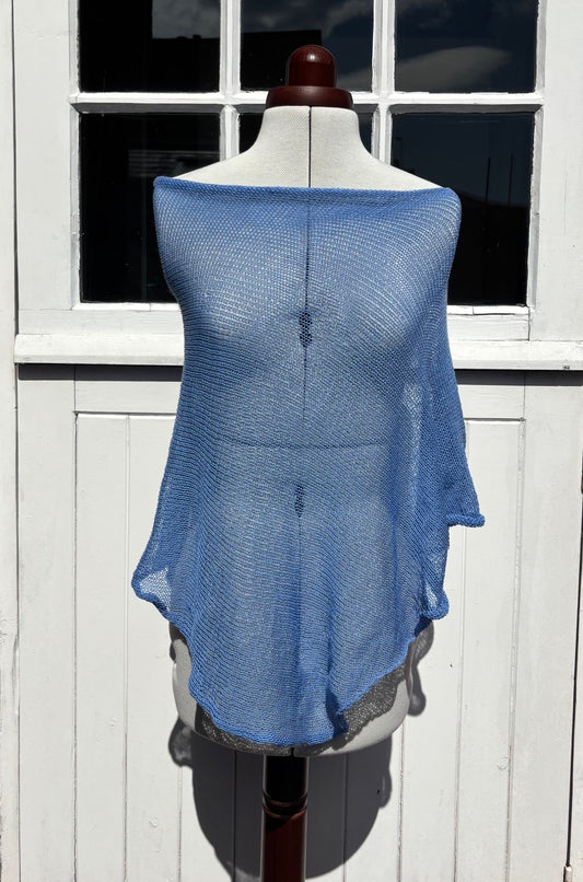 A light blue open-knit shrug or poncho draped over a white dress form mannequin, set against a white wooden paneled door.