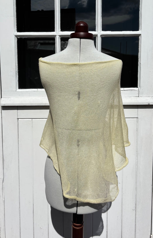 A pale yellow open-knit shawl or wrap draped over a dress form, set against a white paneled window and door background.